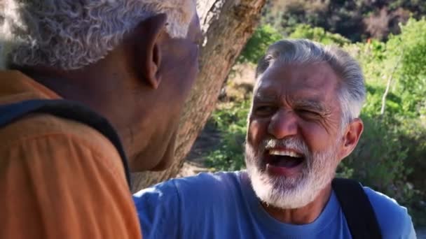 Two senior male friends laughing and talking as they walk along trail through countryside together - shot in slow motion