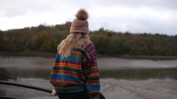 girl with colourful sweater and a beanie hat sitting on a fence looking at the suspension bridge in Bristol.