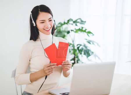 Happy asian young woman  making distance video call and showing red envelope for celebrating chinese new year
