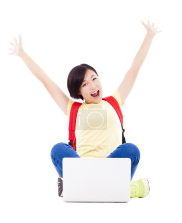兴奋的年轻学生女孩坐在一台笔记本电脑，举起手臂