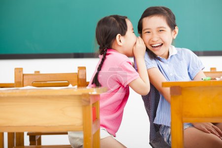 happy little girls whispering and sharing a secret  in classroom