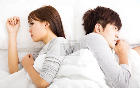 Upset young couple lying side by side in bed