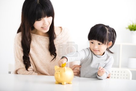 Happy mother and daughter Inserting Coin In Piggy bank