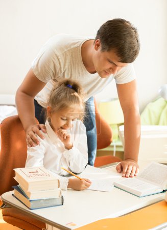 young father looking at daughter doing homework