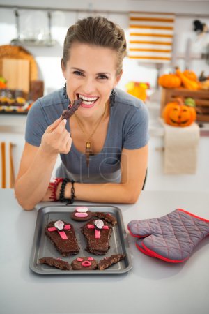 Housewife eating freshly homemade Halloween biscuits in kitchen