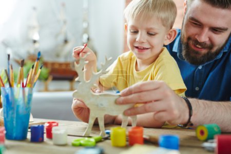 Father with son painting wooden deer