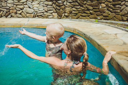 Hipster Mother play with her lovely child in swimming-pool, Bali