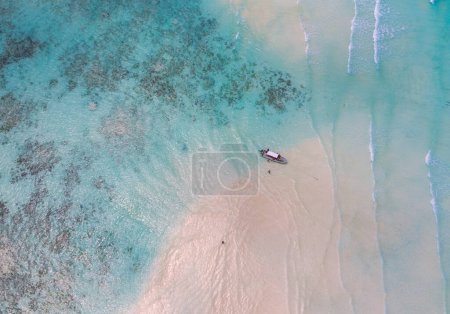 Aerial shot of the Mnemba Island white sand sandbanks washed with turquoise Indian ocean waves near the Zanzibar island, Tanzania. The couple came here on the motorboat, anchored it and having rest.