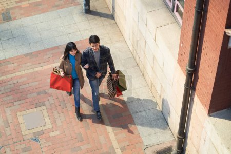 high angle view of young asian couple walking chatting on street with shopping bags in hands