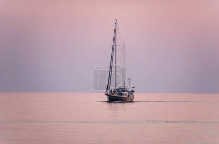 Sailing yacht in the blue sea during beautiful pink sunset. A yacht in peaceful waters.