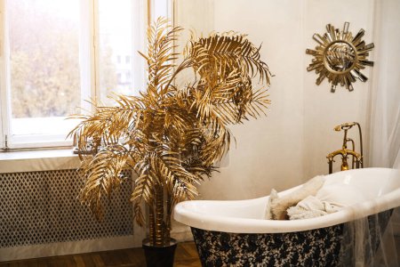 新艺术风格的金棕榈树，靠近浴池。一间有大窗户的房间中央的老式浴室