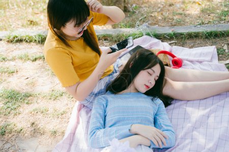 当他们外出野餐时，蓝色的T恤女郎躺在黄色的T恤女郎的膝上，黄色的T恤女郎睡觉时给蓝色的T恤女郎拍照.