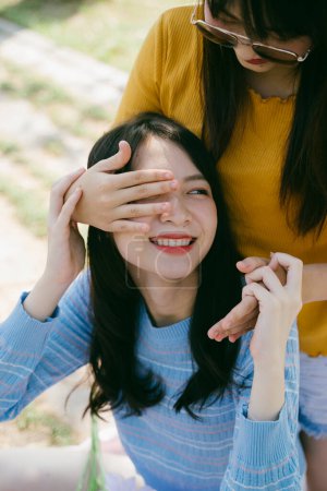两个女孩在公园野餐时玩耍，黄色的T恤衫女孩紧盯着蓝色T恤衫女孩的眼睛.