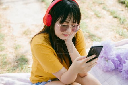 戴太阳镜和红色耳机的黄色T恤女孩在智能手机应用中选择音乐.