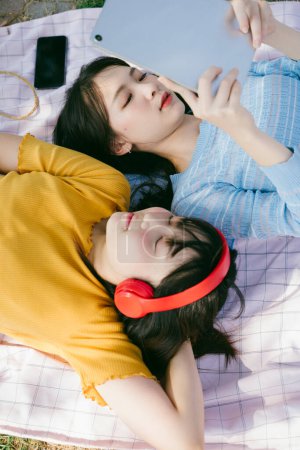 两个女孩躺在垫子上听音乐，用平板电脑.