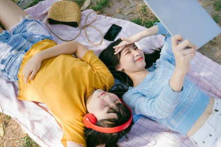 两个女孩躺在垫子上听音乐，用平板电脑.
