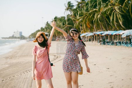 两个活泼的女孩站在海滩上，举手表决.