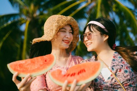 黄昏的时候，两个女孩抱着西瓜在海滩上笑着.