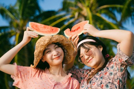 两个可爱的女孩晚上站在海滩上，把西瓜放在头上笑了.