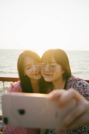 两个长发姑娘在日落前的海边的银色栅栏前自拍.