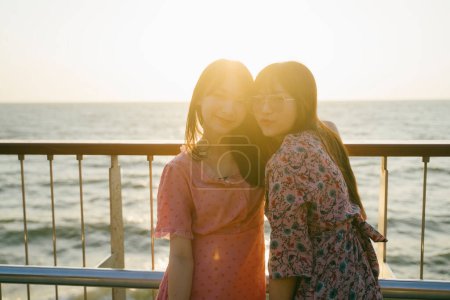 两个长头发的女孩在海边的银色栅栏边拍的侧影.