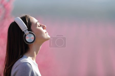 Profile of a woman meditating listening audio on wireless headphones in a pink field