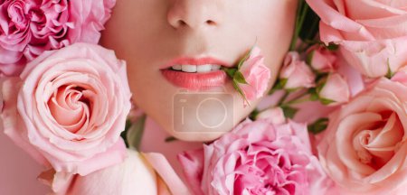 Close up portrait of beautiful woman face wih bright make up and perfect skin posing with many roses on pink background.