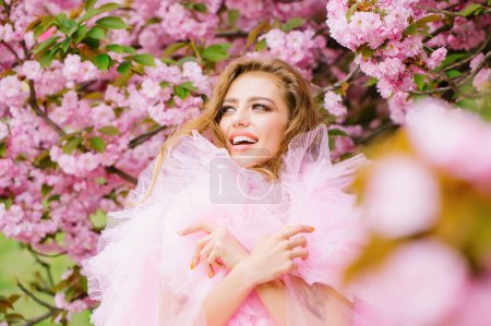 Beautiful young woman in pink glamour dress with smiling face in spring flowers bloom park