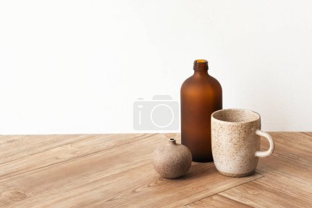 木制地板上的一个褐色花瓶旁边的小咖啡杯