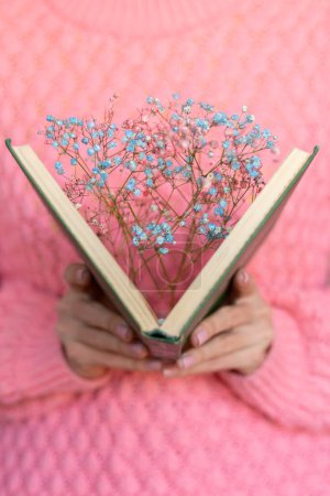 Woman holding an open book with a bouquet of dried flowers inside