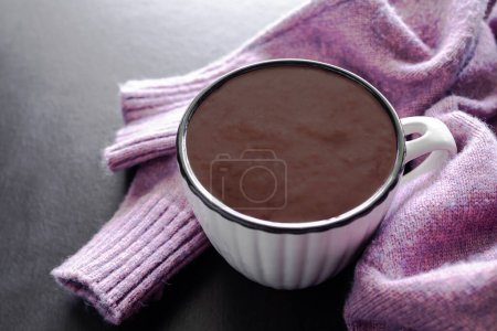 热巧克力牛奶，白色杯子与毛衣外套在黑色木制桌子的背景。世界巧克力日，早餐或放松时间的健康饮料.