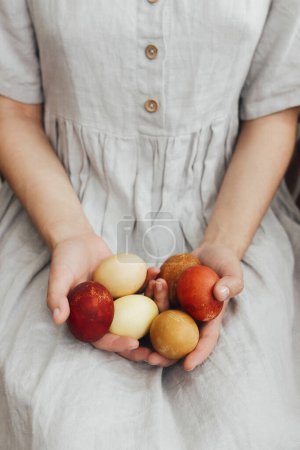 穿着乡村亚麻布衣服的女人手里拿着天然染色的复活节彩蛋。复活节快乐！天然彩绘的生态红蛋和褐色蛋。美感假日，时尚形象