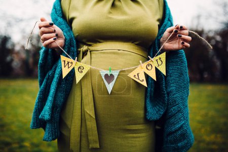 close-up shot of pregnant woman holding garland with we love you inscription