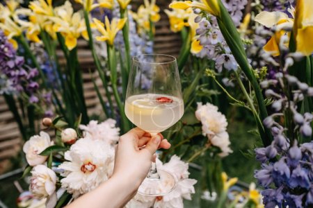 cropped shot of woman holding glass of cocktail in front of flowers