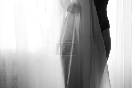 Female silhouette hiding behind tulle curtain. Black and white photography