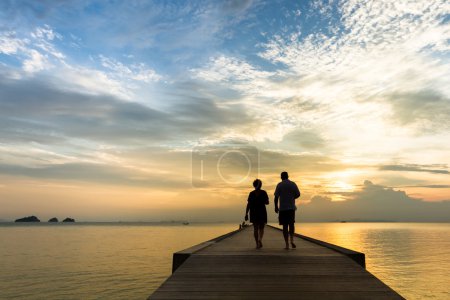 Elderly couple walking on the pier at sunset on a tropical island