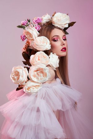 Beauty Woman bright red makeup, rose flowers on head woman. Art Girl in a transparent light dress on a pink background. Professional bright makeup