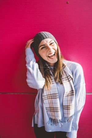 Woman wearing hat leaning on pink wall 