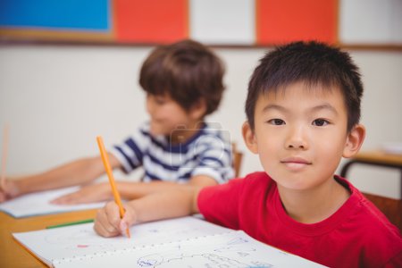 Cute pupils drawing at their desks one smiling at camera