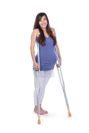 Full length portrait of a smiling pregnant woman using crutch ,
