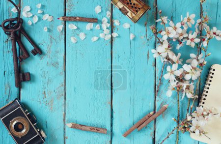 Top view image of spring white cherry blossoms tree, blank notebook, old camera on blue wooden table