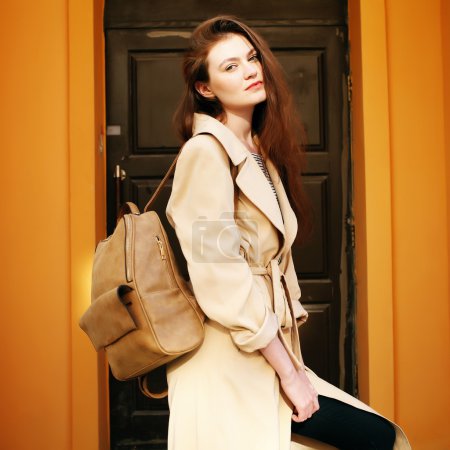 Young stylish hipster girl wearing modern trench coat walking in urban city smiling happy. 