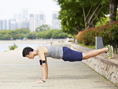 Young asian man doing pushups in park