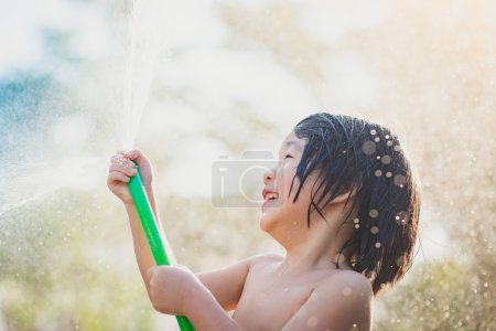 Cute asian boy has fun playing in water from a hose outdoors