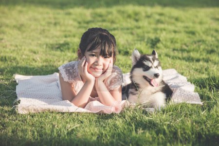 Beautiful asian girl lying on green grass with a siberian husky