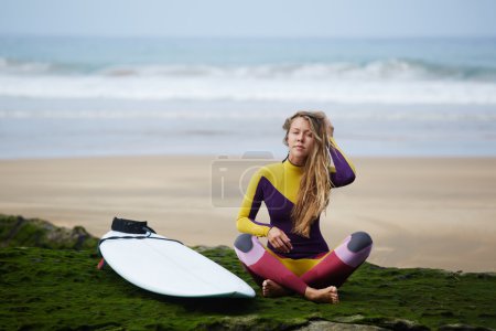骑一个冲浪板亮穿裙子的女孩坐在沙滩上后被征服波