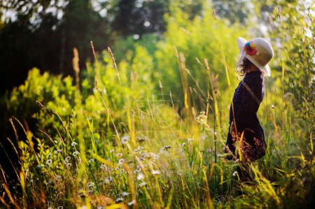 Dreamy child girl on summer walk on riverside. Cozy rural scene. Outdoor activities on summer vacations.