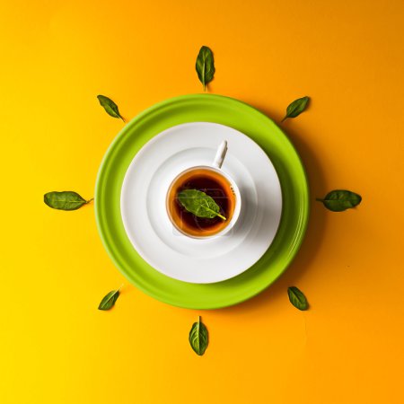 Tea in a cup with green leaves  on orange background.